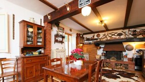 Un coin repas rustique avec une table et des chaises en bois, un buffet aux portes vitrées et une cheminée agrémentée d’un tapis en peau de vache.