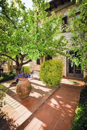 Une cour avec un bâtiment en pierre, un grand arbre et une plante en pot.