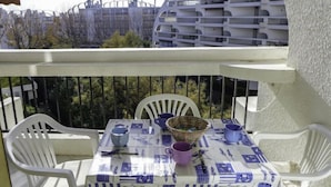 A balcony with a table set for two, white chairs, and a view of a modern building with balconies. - Ulysse Plage by Interhome (La Grande Motte)