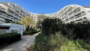 A modern, curved building with multiple balconies, surrounded by greenery and a clear sky. - Ulysse Plage by Interhome (La Grande Motte)