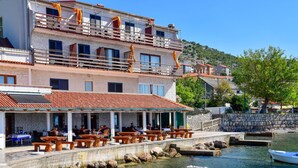 A waterfront restaurant with outdoor seating, a stone wall, and boats docked nearby. - Apartment Val by Interhome (Sveti Juraj)