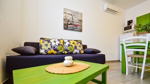 A modern living room with a green table, a sofa with floral cushions, and a painting of a harbor scene. - Apartment Val by Interhome (Sveti Juraj)