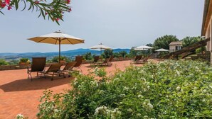 Un área de estar al aire libre con tumbonas y sombrillas, rodeada de abundante vegetación y vistas a montañas lejanas.