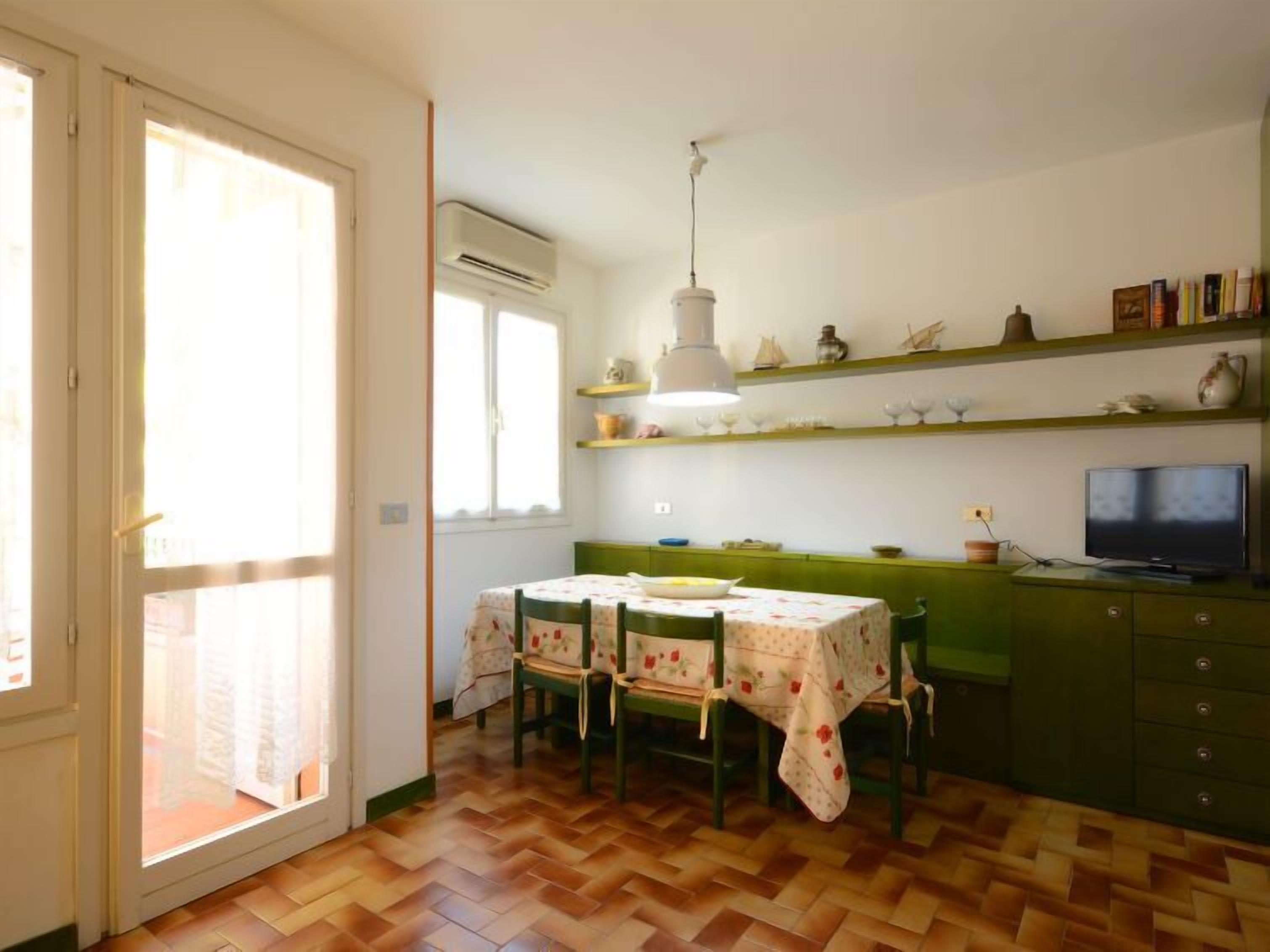 A dining area with a table set for four, a television on a cabinet, and a window with blinds.