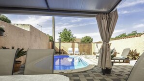 Et overdækket udendørs område med swimmingpool, liggestole og et pergola.