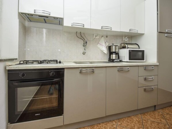 A kitchen with white cabinets, a stove, an oven, a microwave, and a coffee maker.