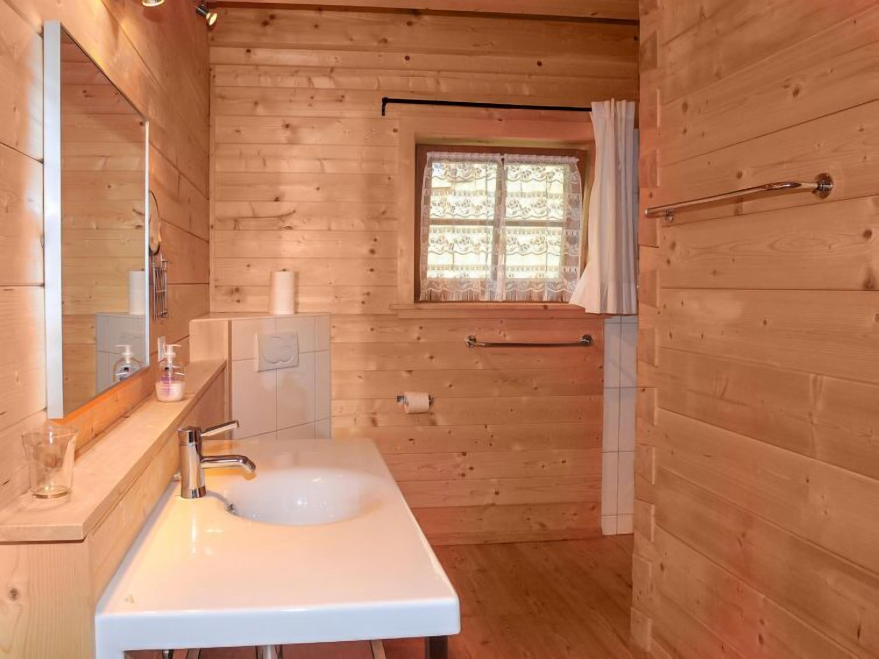Baño de cabaña de madera con lavamanos, espejo, ventana y ducha.