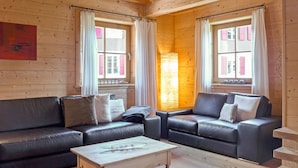 A cozy room with two leather sofas, a wooden coffee table, and large windows with curtains. - Alpina Apt. CH by Interhome (Wengen)