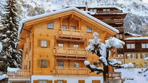 A wooden chalet with multiple balconies, surrounded by snow-covered mountains. - Alpina Apt. CH by Interhome (Wengen)