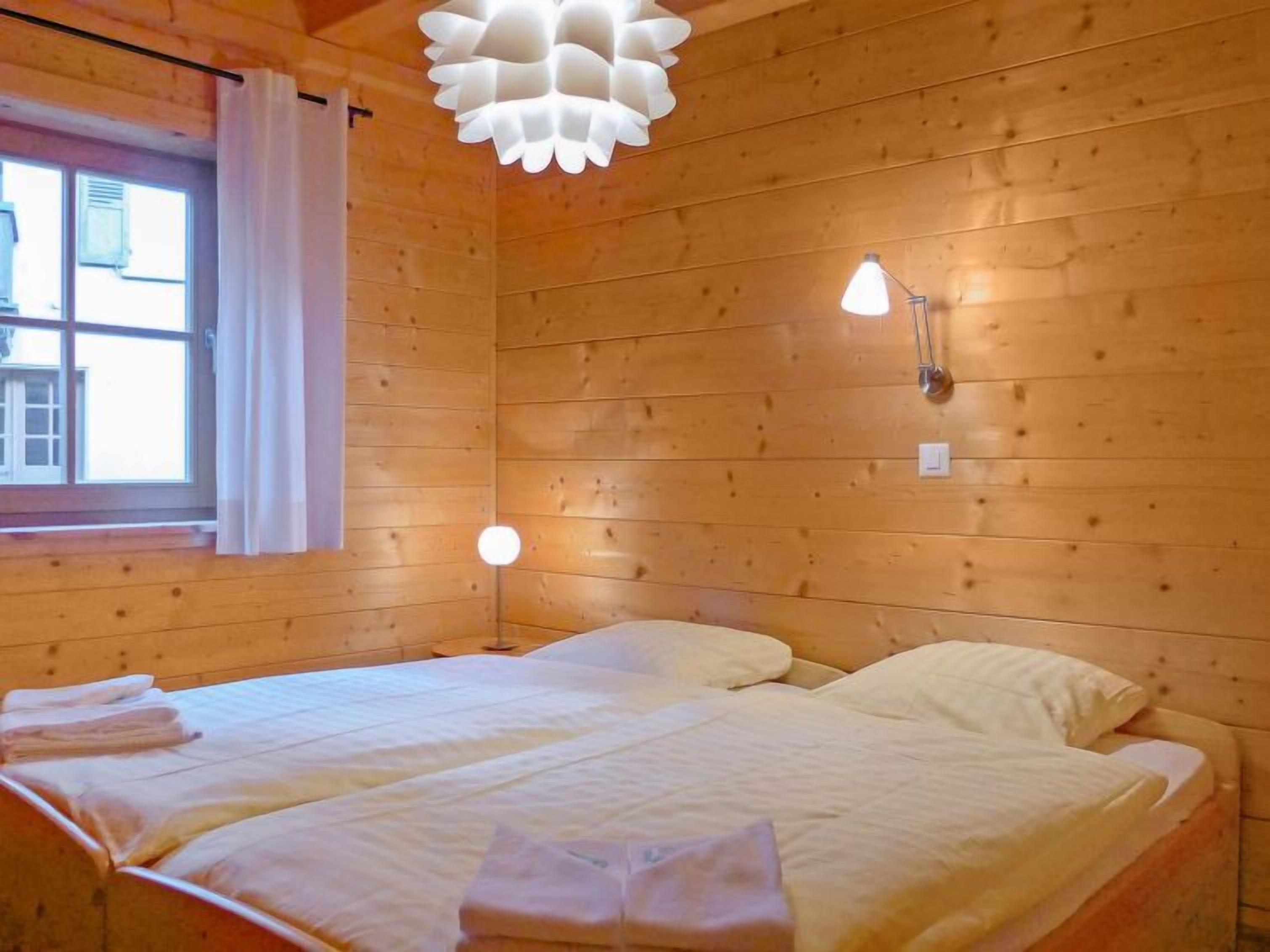 Ein Zimmer aus Holz mit Bett, einem Fenster mit Vorhängen und einer modernen Lampe.