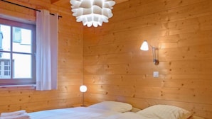 A wooden room with a bed, a window with curtains, and a modern light fixture. - Alpina Apt. CH by Interhome (Wengen)