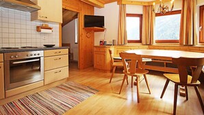 A cozy kitchen with wooden cabinets, a stove, and a dining area with a table and chairs. - Apartment Werner by Interhome (Pettneu am Arlberg)