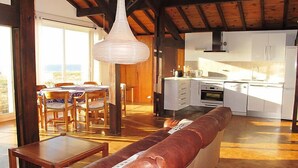 A spacious living area with a long leather sofa, wooden dining table, and chairs. A kitchen with white cabinets and appliances is visible in the background. - Apartment Capama by Interhome (Mimizan)