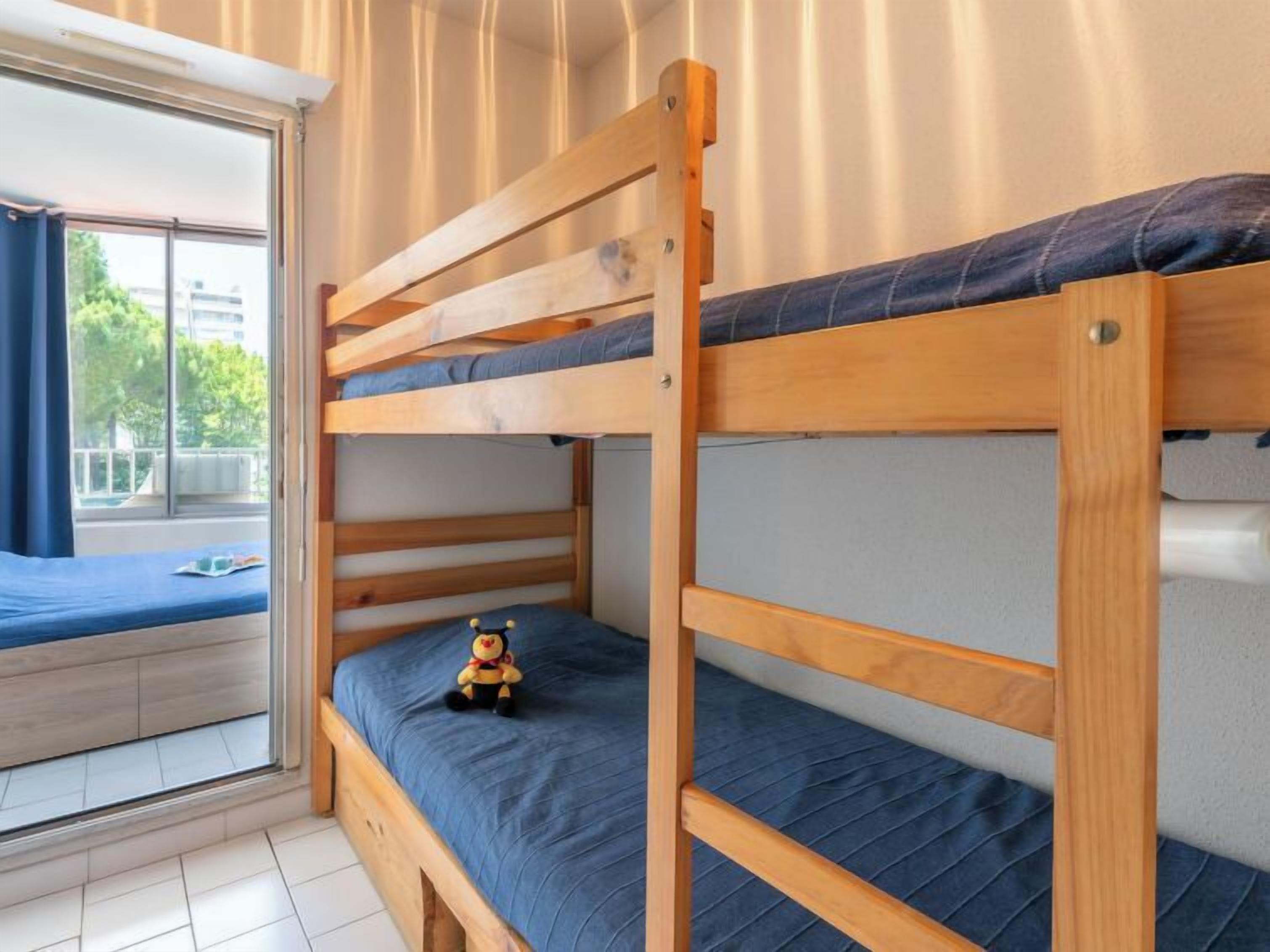 A room with two bunk beds, a window with curtains, and a view of greenery outside.