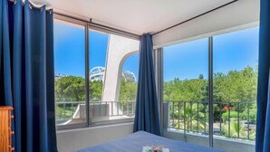 Een hotelkamer met een groot bed, uitzicht op een modern gebouw en een balkon met een leuning.