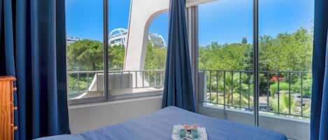 A hotel room with a large bed, a view of a modern building, and a balcony with a railing.