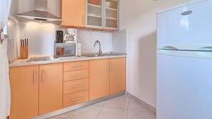 Une cuisine compacte équipée d’un four à micro-ondes, d’une cuisinière et d’un évier. On y trouve un meuble avec des tiroirs et, au-dessus de la cuisinière, un meuble avec des portes en verre.