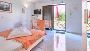 Une chambre d’hôtel comprenant un lit, une télévision, un coin repas avec des chaises et une table, ainsi qu’un balcon équipé d’un parasol.