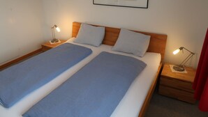Un lit double avec deux oreillers, une œuvre d’art abstraite encadrée au-dessus, et deux tables de chevet avec des lampes.