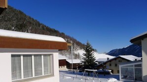 Un espace extérieur enneigé, avec des bâtiments, une structure en bois et une montagne en arrière-plan.