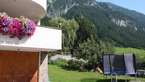 A balcony with hanging flowers, a wooden door, and a view of a mountainous landscape. - Christian by Interhome (Pettneu am Arlberg)