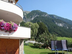 A balcony with hanging flowers, a wooden door, and a view of a mountainous landscape. - Christian by Interhome (Pettneu am Arlberg)