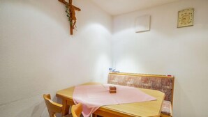 A dining area with a wooden table, four chairs, a pink tablecloth, a wooden bench with a cushion, a wall-mounted cross, and a framed picture. - Christian by Interhome (Pettneu am Arlberg)