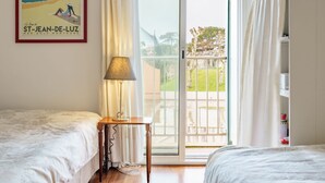 Una habitación de hotel con dos camas, una mesa con lámpara, una ventana con cortinas y un cartel en la pared.