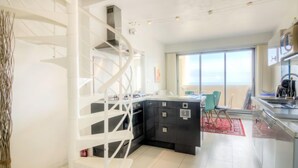 Une cuisine moderne avec un îlot central, un coin repas agrémenté d’un tapis rouge et un balcon avec vue.