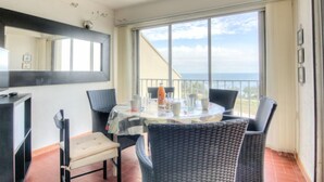 Un balcon avec une table et des chaises, une grande fenêtre et une vue sur la mer.