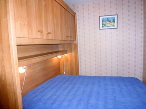 Een slaapkamer met een stapelbed, een houten garderobe en een klein, ingelijst foto aan de muur.