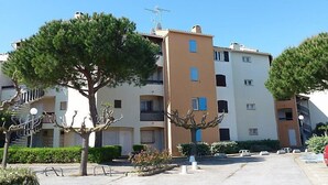 Un immeuble résidentiel à plusieurs étages, doté de balcons, avec un ciel dégagé et entouré de verdure.