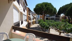 Un balcon avec une table et des chaises, donnant sur une cour intérieure agrémentée d’arbres et de bâtiments.