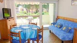 Un coin repas avec une table dressée pour quatre personnes, un canapé bleu et un téléviseur posé sur un meuble en bois.