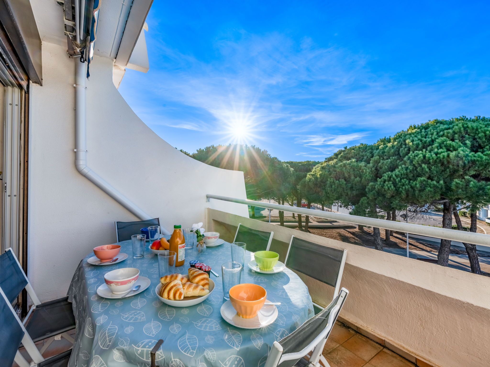 A balcony with a table set for breakfast, overlooking a tree-lined area.