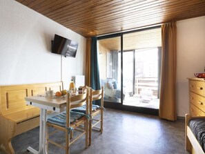 Une pièce avec un plafond en bois, un téléviseur fixé au mur, un lit, un bureau avec une chaise et une fenêtre avec des rideaux.