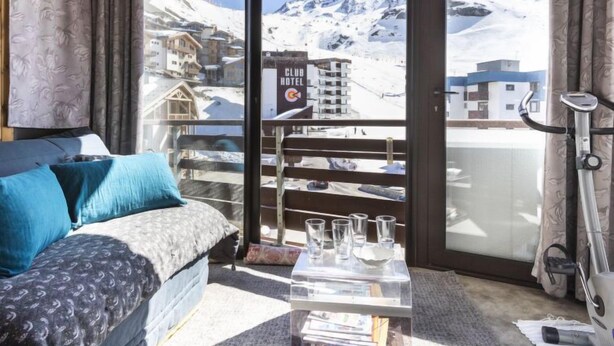 A room with a bed, a glass coffee table, and a view of snow-covered mountains and buildings. - Schuss 309 by Interhome (Val Thorens)