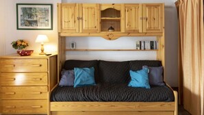 A cozy room with a wooden sofa, a wooden dresser, and a shelf with books and a small decorative item. - Schuss 309 by Interhome (Val Thorens)