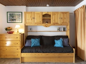 A cozy room with a wooden sofa, a wooden dresser, and a shelf with books and a small decorative item. - Schuss 309 by Interhome (Val Thorens)