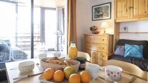 A cozy room with a wooden ceiling, a dining table with breakfast items, a sofa, and wooden cabinets. - Schuss 309 by Interhome (Val Thorens)