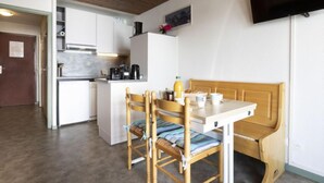 A compact kitchen with white cabinets, a wooden bench, and a television mounted on the wall. - Schuss 309 by Interhome (Val Thorens)
