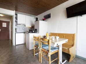 A compact kitchen with white cabinets, a wooden bench, and a television mounted on the wall.