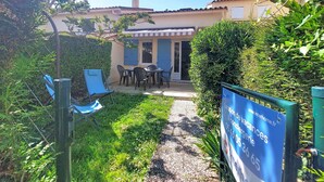 Une cour avec une table et des chaises, un espace de repos couvert et un panneau indiquant les coordonnées.