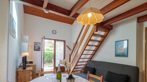 Un coin repas avec une table ronde dressée pour quatre personnes, un escalier en bois, un canapé et une fenêtre donnant sur un paysage verdoyant.