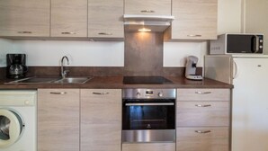 Une cuisine compacte dotée de meubles en bois, d’un four encastré, d’un four à micro-ondes, d’une machine à café et d’un lave-linge.