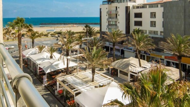 Hotel met uitzicht op het strand, buitenterras en palmbomen.