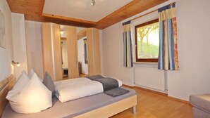 A modern bedroom with a wooden ceiling, a bed with pillows, a window with curtains, and a view of the outdoors.
