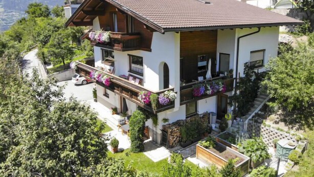 A multi-story chalet with balconies, a patio area, and a view of the surrounding mountains.