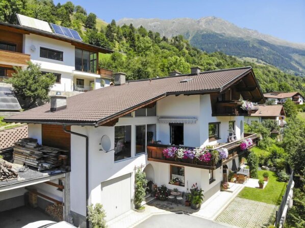 Une maison moderne à deux étages, dotée d’un toit en pente, de grandes fenêtres et d’un balcon agrémenté de plantes en pot.