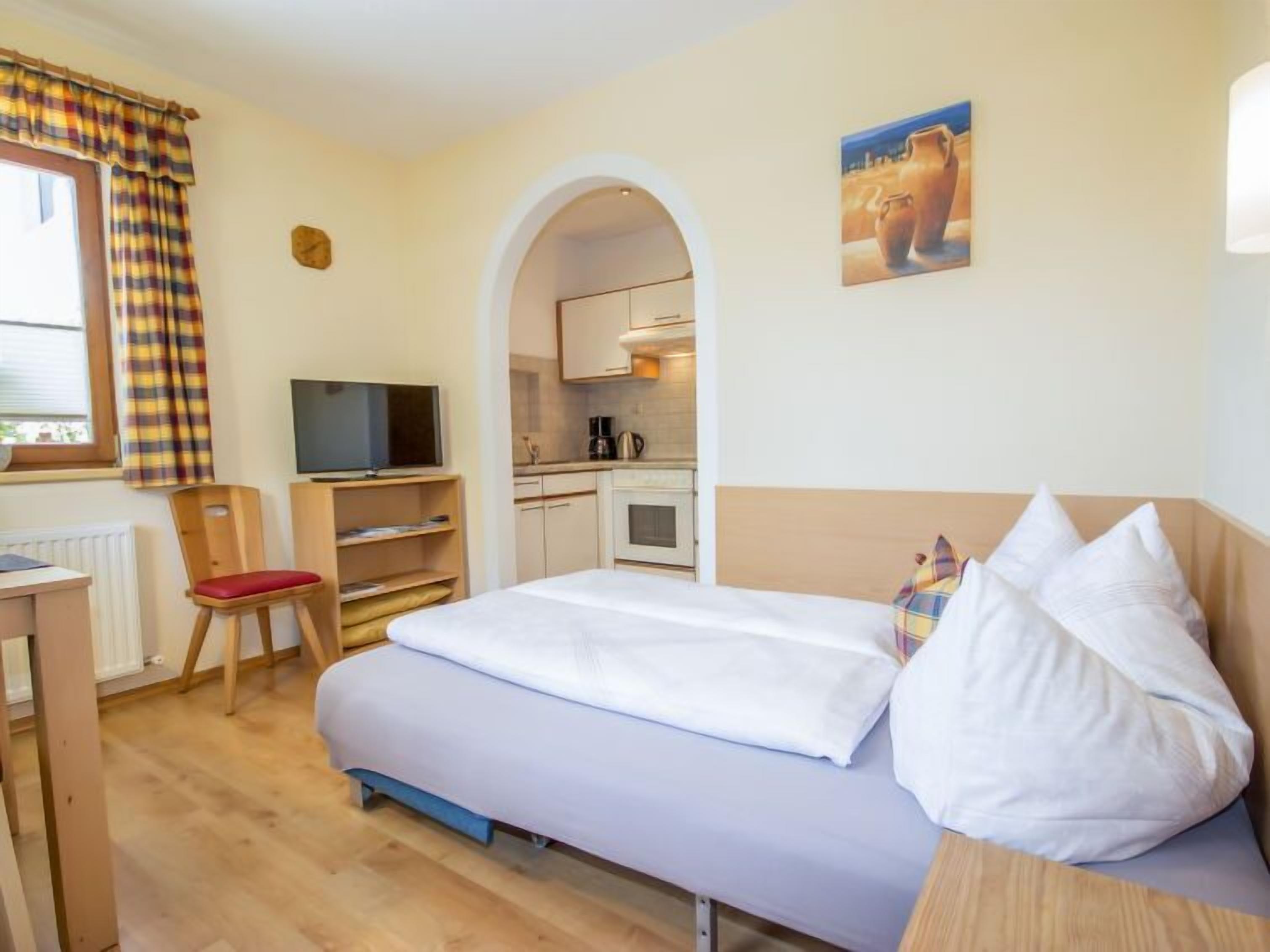 Een hotelkamer met een bed, een bureau, een stoel, een televisie, een kitchenette en een schilderij aan de muur.